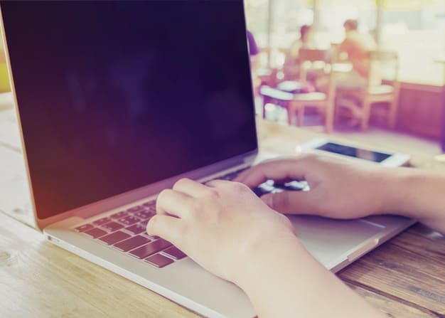 Hands typing on a laptop keyboard while researching online courses. The scene is a close-up, focusing on the keyboard and screen, with a blurred background to emphasize the action.
