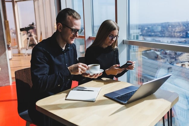 Business people discussing economic forecast charts in a modern office setting, with laptops and coffee cups on the table. The room has large windows with a city view.
